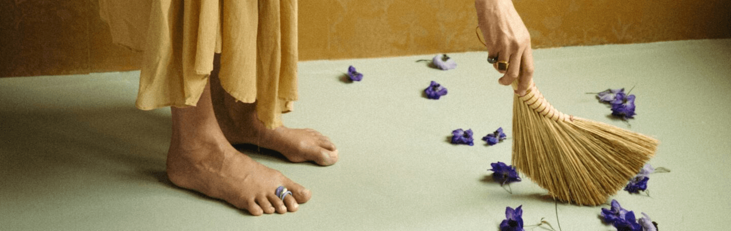 brede foto van een paar voeten, er liggen bloemen op de vloer en een hand met een vegertje veegt die aan de kant